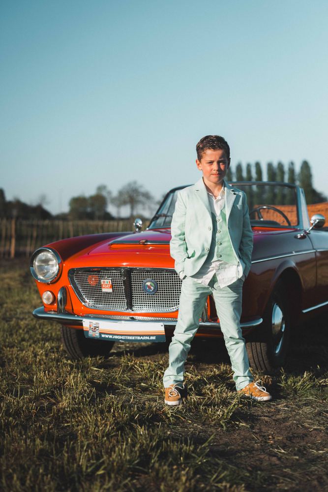Communicant in pak bij een oldtimer